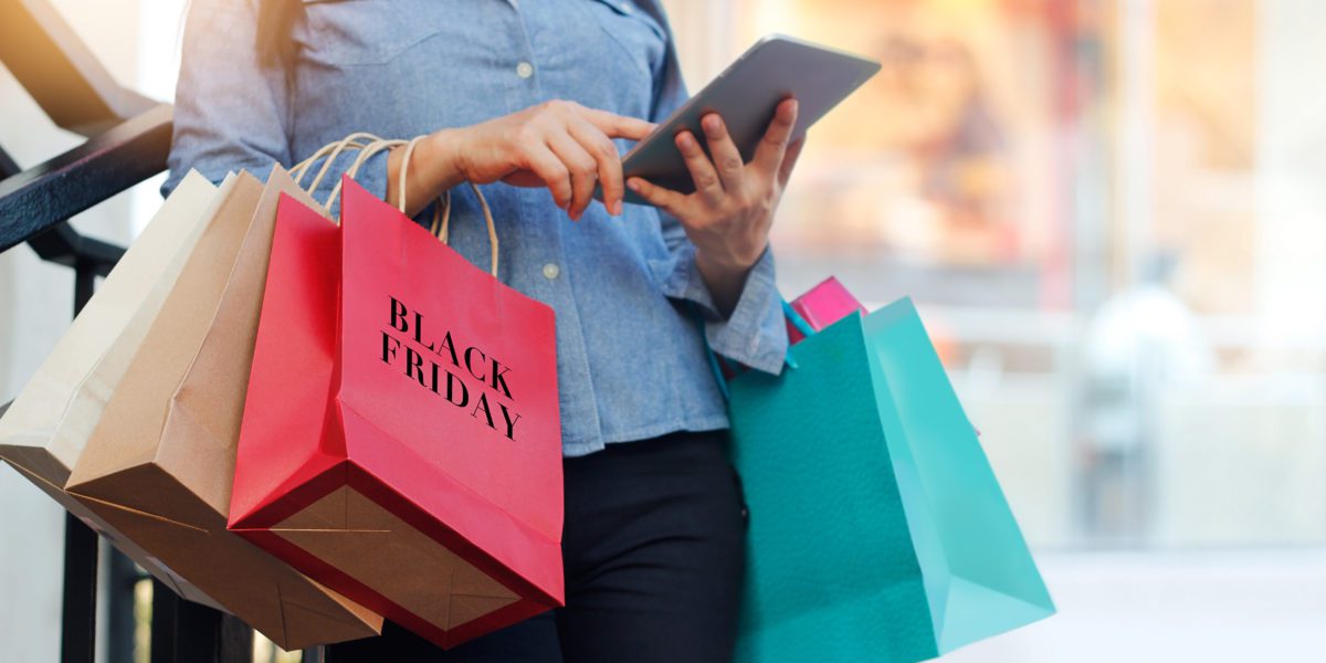 Woman using tablet and holding Black Friday shopping bag